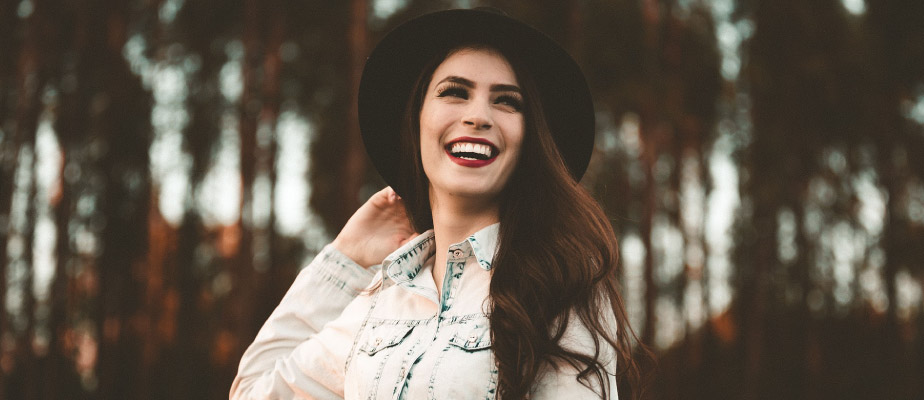 woman with long brunette hair wearing a black hat and denim shirt smiling and looking away