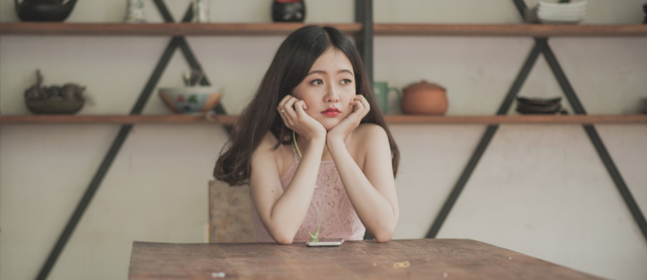 young woman with long dark hair, resting chin in hands, sitting at wooden table