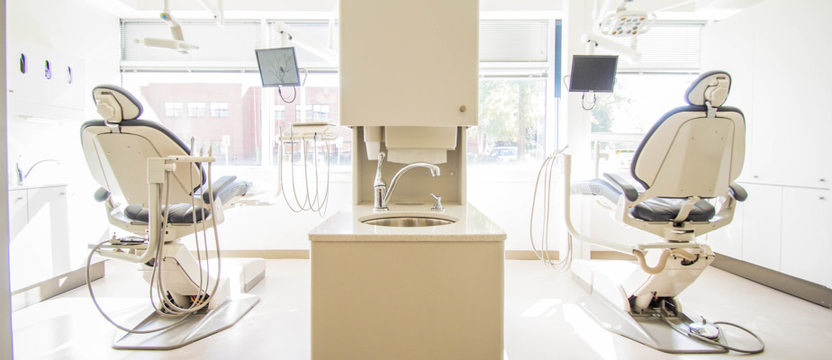 A structure with a faucet and sink separates two cubicles with dental chairs at a dental office