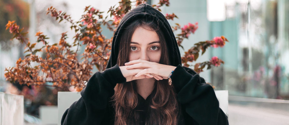 Brunette woman wearing a black hoodie covers her mouth with her hands due to embarrassing yellow teeth