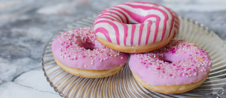 Closeup of a stack of 3 donuts covered in pink and white icing and sprinkles on a clear wavy plate on a gray counter