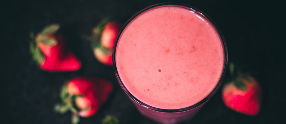 Aerial view of a strawberry protein shake with uncut strawberries clustered around it