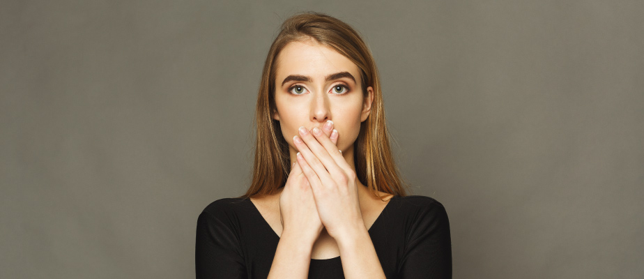 Blonde woman wearing a black shirt covers her mouth with her hands because she is embarrassed about her overbite