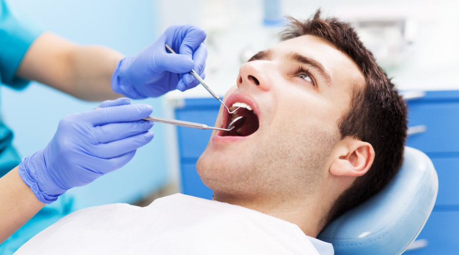 Brunette man sits in a dental chair as a dental hygienist examines his mouth with modern dentistry tools