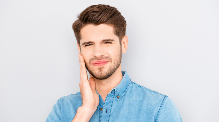 Brunette man cringes in pain and touches his cheek due to an untreated abscess