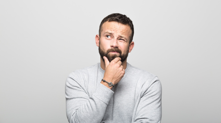 Brunette man with facial hair in a gray shirt strokes his chin while wondering if he needs root canal therapy