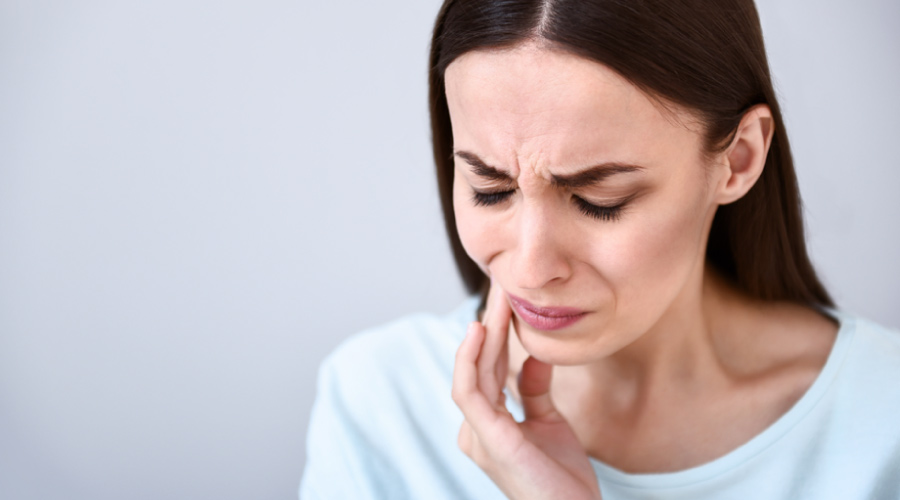 Brunette woman cringes in pain and touches her cheek due to a toothache