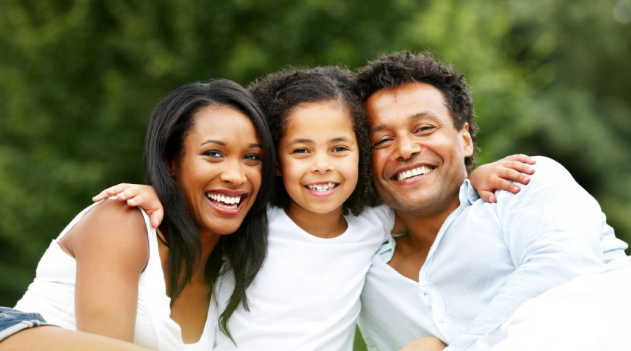 Black mother, daughter and father smiling in front of green trees