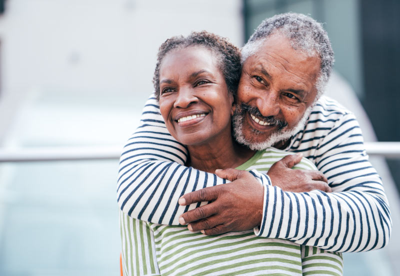 Smiling older black couple with the man standing behind the woman and enfolding her in his arms