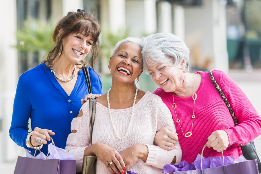 Three older ladies with linked arms, smiling and shopping together