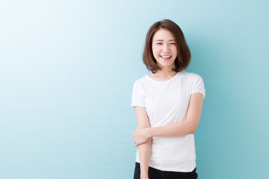 Brunette woman in a white t-shirt smiles against a blue wall after teeth whitening in Elk Grove, CA