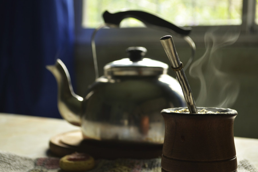A coffee pot on a counter with window in the background and a steaming mug of yerba coffee alternative in the foreground