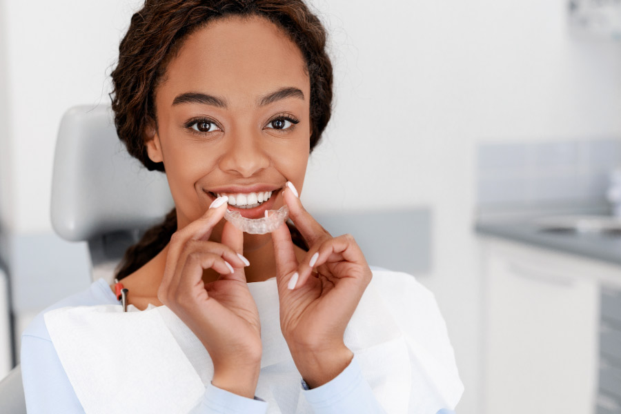 Pretty black girl is holding a ClearCorrect® clear aligner in front of her smile.