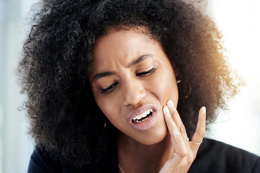 Dark haired woman with her fingers to her cheek because of tooth pain.