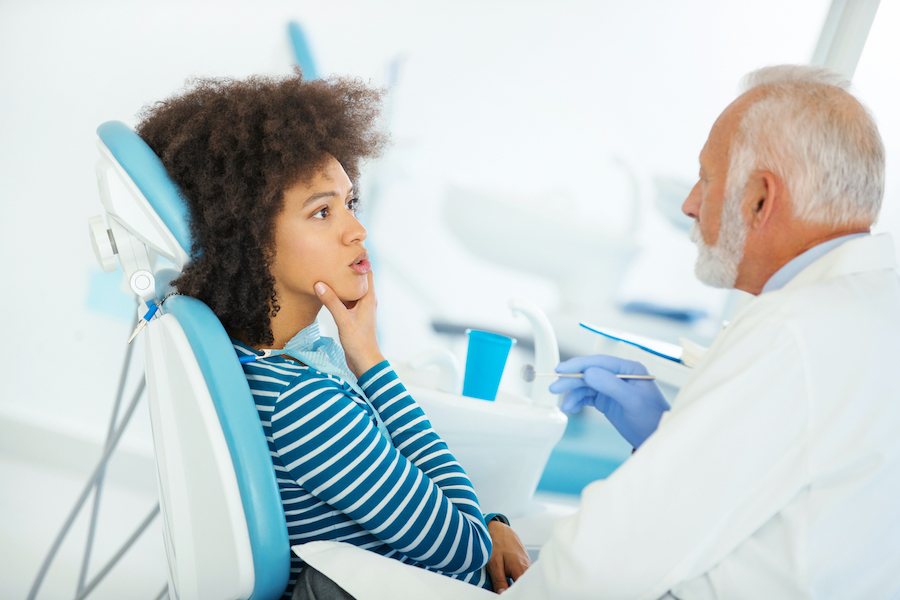 Black woman in a striped shirt talks about oral surgery with her dentist