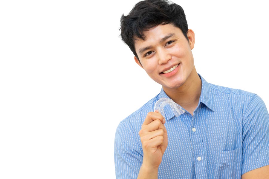 young man smiles as he holds up his clear aligner
